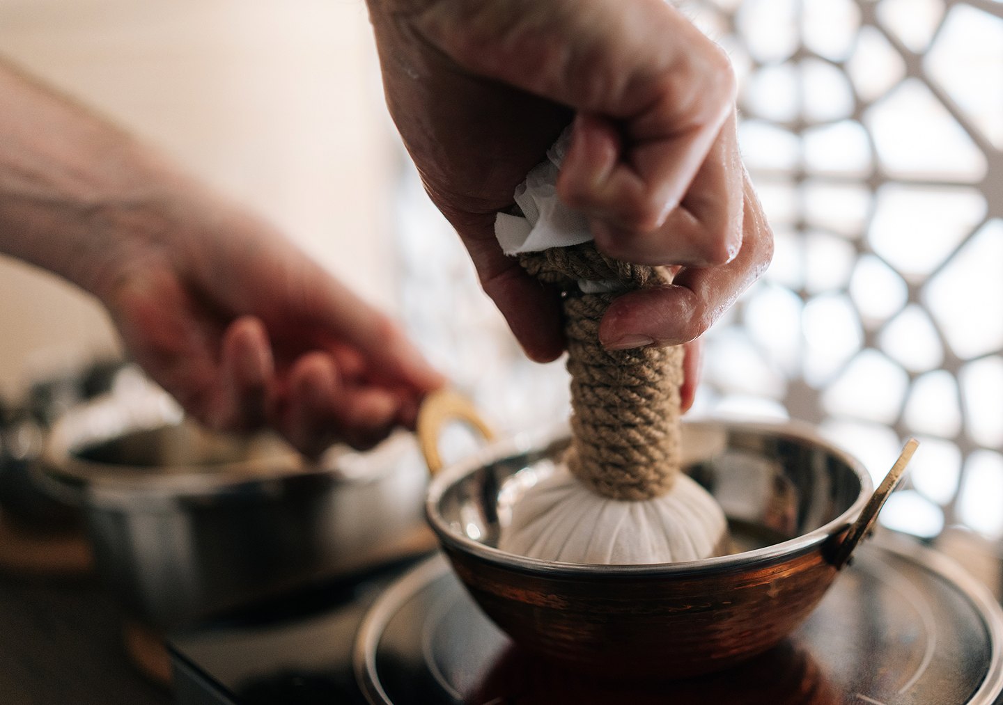 An Ayurvedic ritual: a warm herbal poultice is dipped into a brass bowl of oil.